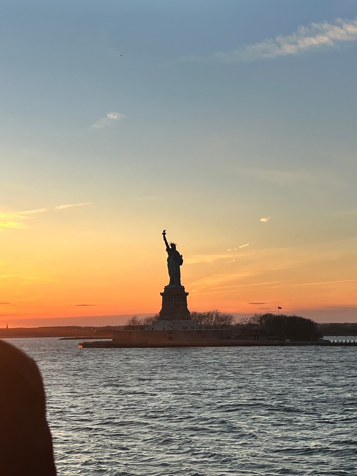 Statue of Liberty silhouetted against a sunset over the water